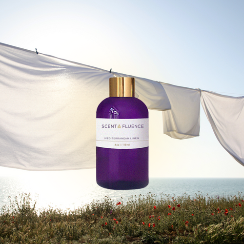 ScentFluence purple bottle with gold cap against a scenic background with clean linen drying in the sunshine over the Meditteranen and flowers in the foreground.