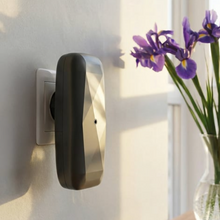 Load image into Gallery viewer, SMI DIAMOND scent diffuser in black plugged into wall outlet. besides window and glass vase with purple iris flowers